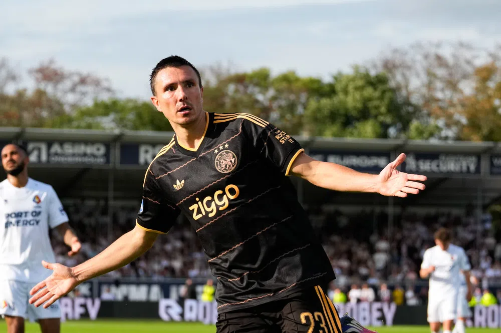 Ajax-speler in zwart uittenue juicht op het veld tijdens een wedstrijd.