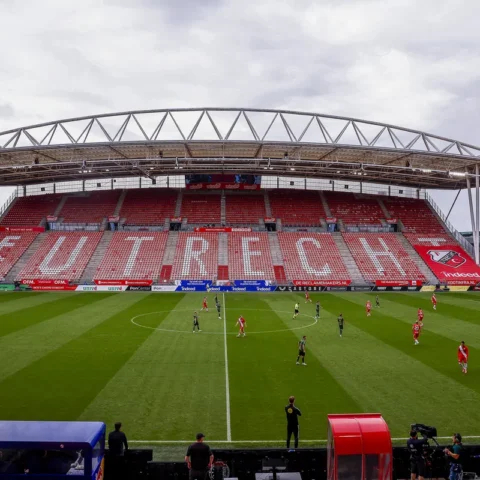 Een voetbalwedstrijd in Stadion Galgenwaard met lege rood-witte tribunes en spelers op het veld.