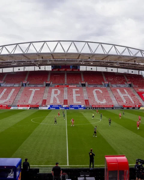 Een voetbalwedstrijd in Stadion Galgenwaard met lege rood-witte tribunes en spelers op het veld.