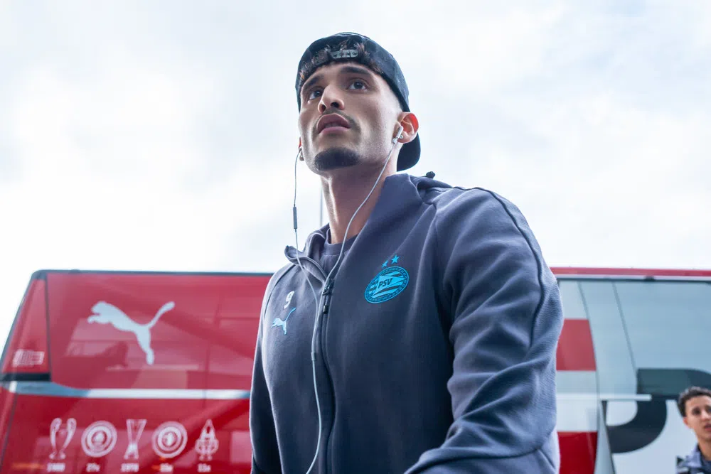 PSV-speler in clubtrainingspak met oordopjes voor een PSV-teambus.