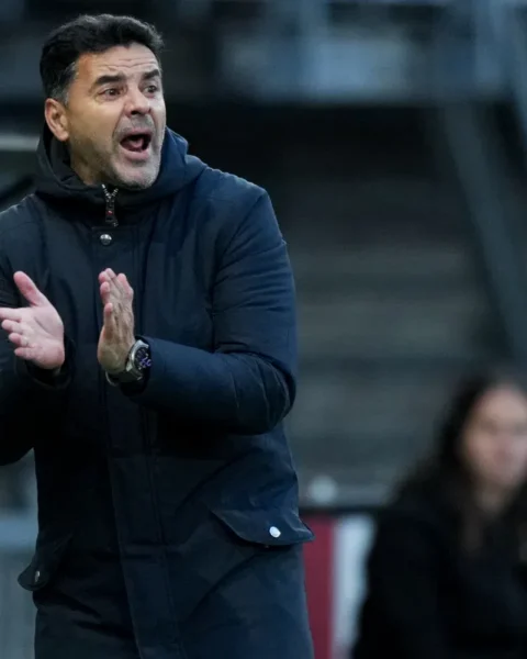 Míchel staat langs de zijlijn en klapt tijdens een voetbalwedstrijd.