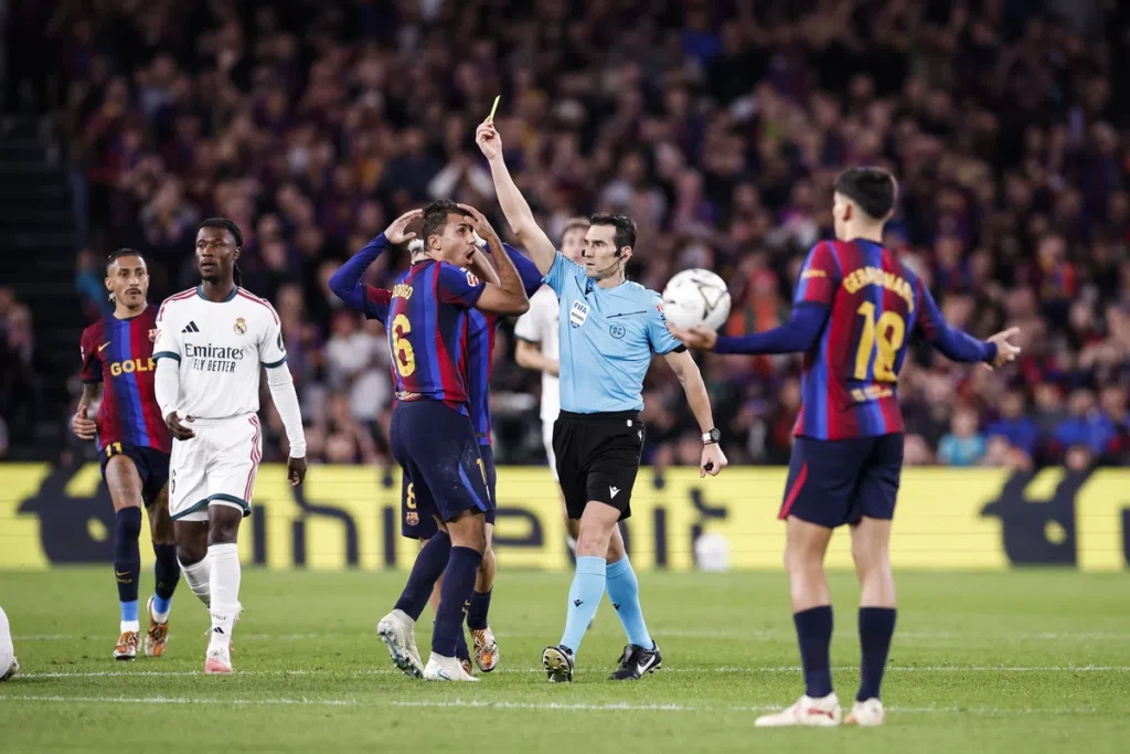 Scheidsrechter met een gele kaart tussen spelers tijdens een La Liga-wedstrijd.