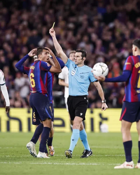 Scheidsrechter met een gele kaart tussen spelers tijdens een La Liga-wedstrijd.