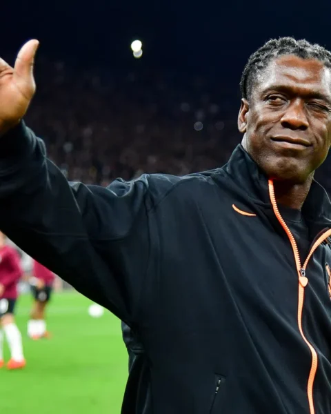 Clarence Seedorf steekt zijn hand op langs het veld voor een voetbalwedstrijd.