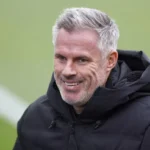 Jamie Carragher glimlacht tijdens een interview op een voetbalveld.