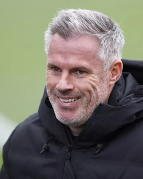 Jamie Carragher glimlacht tijdens een interview op een voetbalveld.