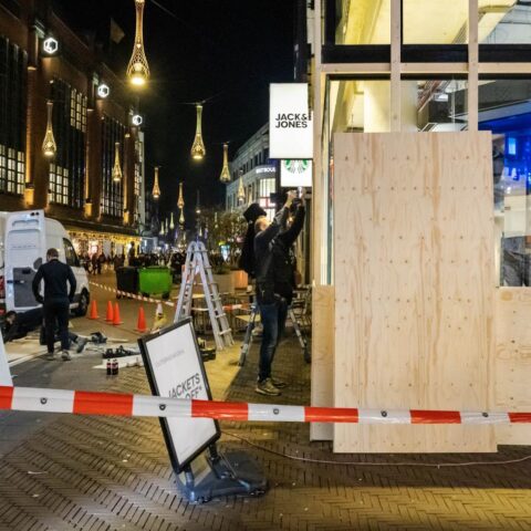 Winkelpui in The Hague wordt ’s avonds dichtgetimmerd terwijl mensen planken plaatsen en afzetlint de straat afsluit.