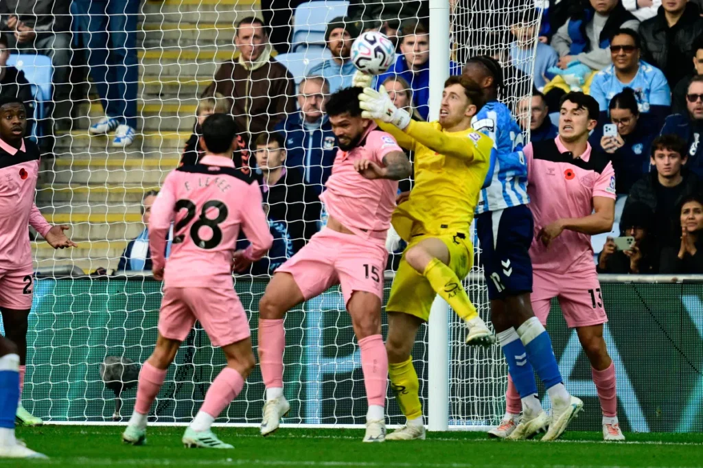 Keeper in geel en spelers in roze en blauw springen bij het doel om de bal.