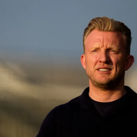 Dirk Kuijt staat buiten in het zonlicht met een stadion op de achtergrond.
