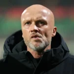 Dick Schreuder staat langs het veld in een zwarte jas.