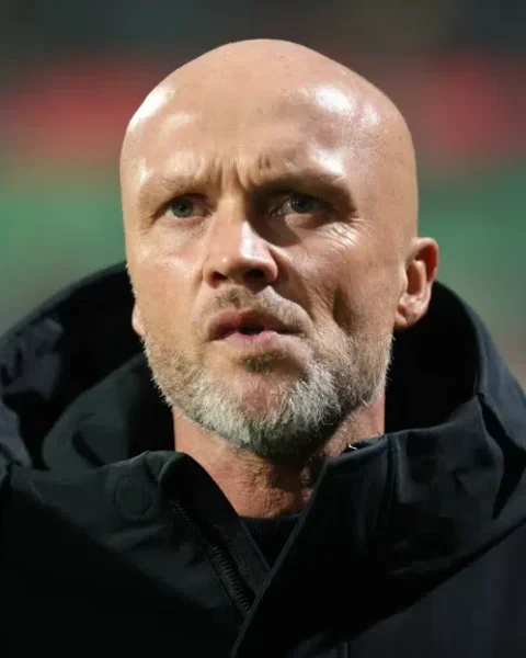 Dick Schreuder staat langs het veld in een zwarte jas.