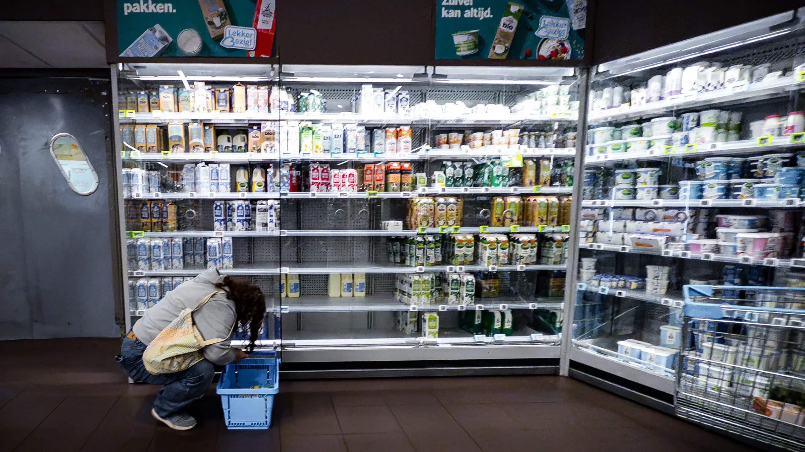 Een klant bukt voor een vrijwel lege koelvitrine in een Albert Heijn-winkel.