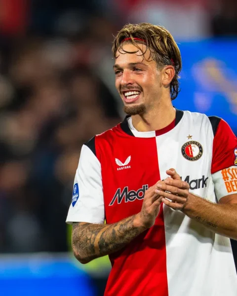 Feyenoord-speler in rood-wit tenue op het veld, klappend en lachend.
