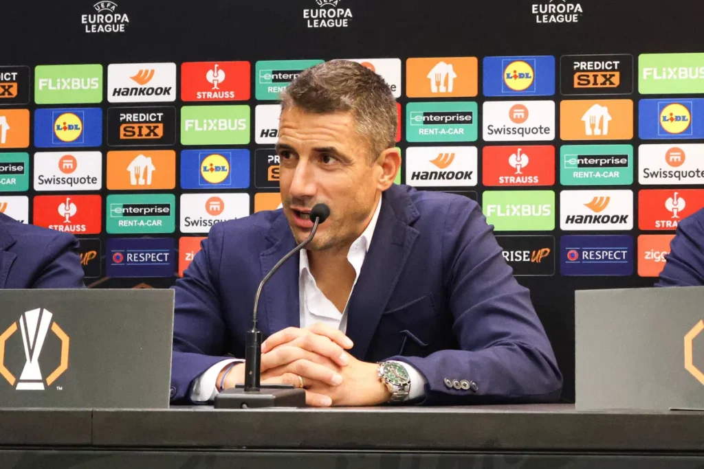 Julio Velázquez spreekt tijdens een Europa League-persconferentie achter een microfoon.