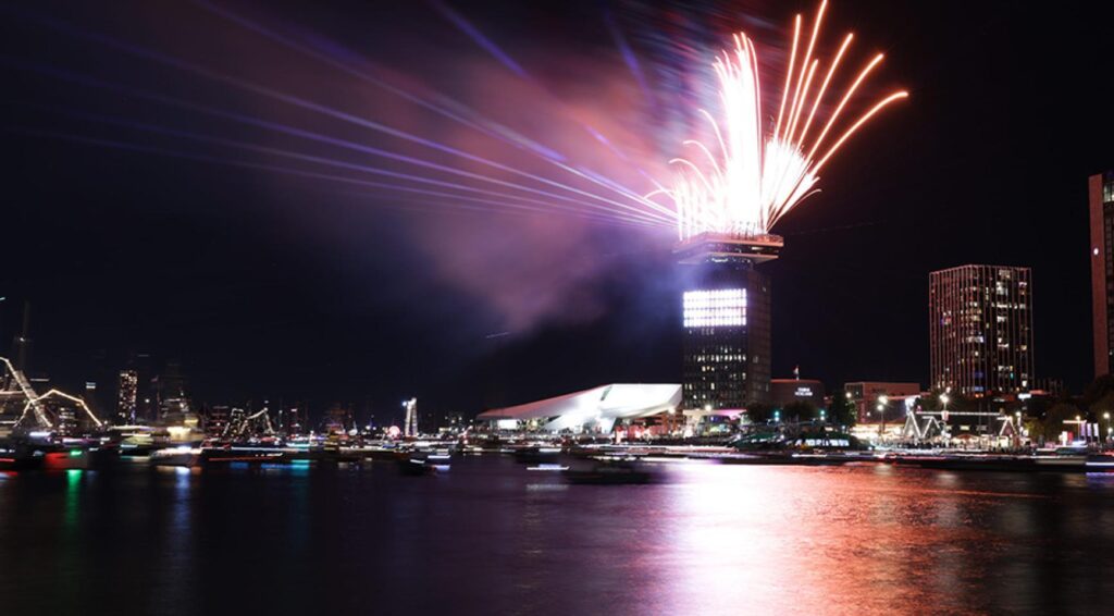 Vuurwerk boven een stad aan het water bij nacht.