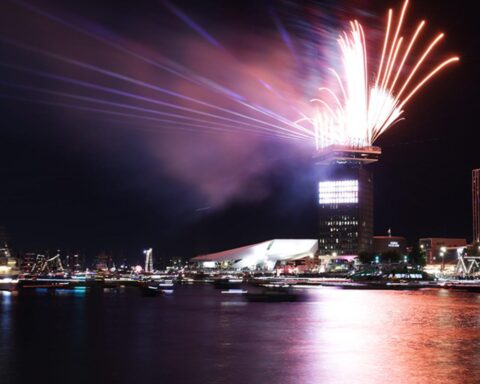 Vuurwerk boven een stad aan het water bij nacht.