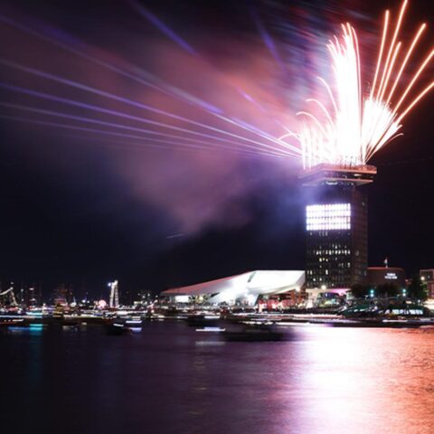 Vuurwerk boven een stad aan het water bij nacht.