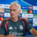 José Mourinho zit aan een persconferentietafel in een Real Madrid-shirt voor een sponsorwand.
