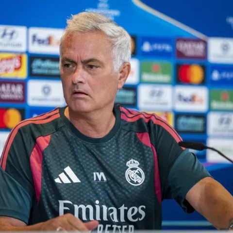 José Mourinho zit aan een persconferentietafel in een Real Madrid-shirt voor een sponsorwand.