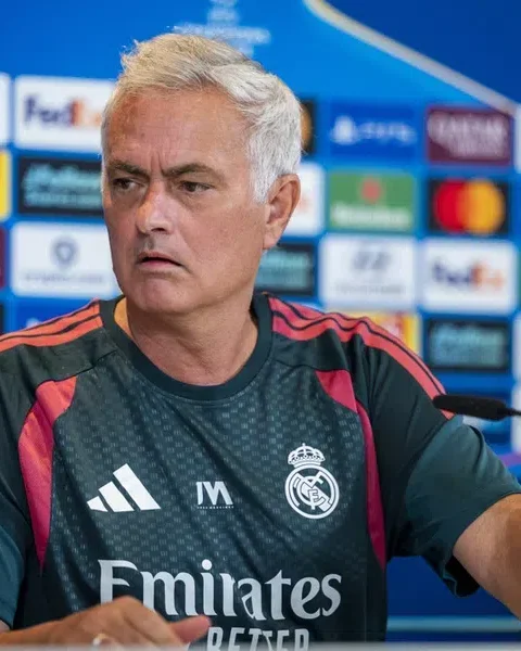 José Mourinho zit aan een persconferentietafel in een Real Madrid-shirt voor een sponsorwand.
