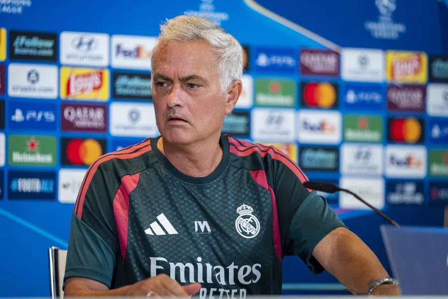 José Mourinho zit aan een persconferentietafel in een Real Madrid-shirt voor een sponsorwand.