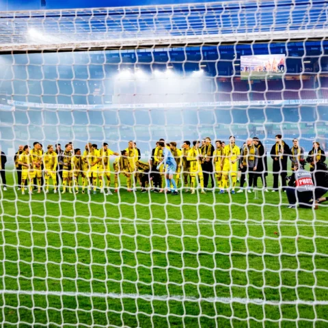 Bodø/Glimt-spelers staan op het veld in het Aspmyra Stadion, gezien door het doelnet.