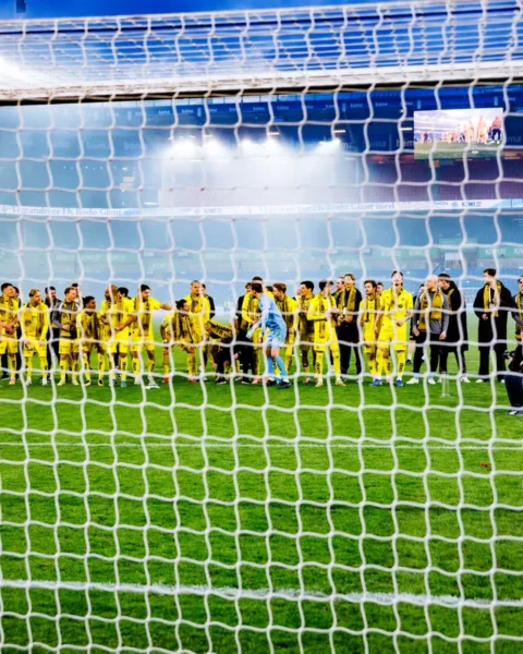 Bodø/Glimt-spelers staan op het veld in het Aspmyra Stadion, gezien door het doelnet.