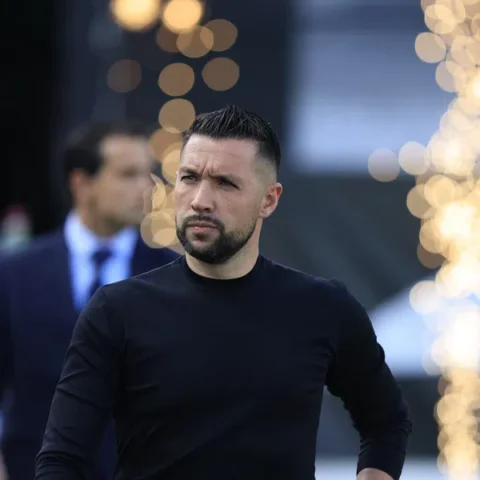 Francesco Farioli staat bij een voetbalwedstrijd met een donkere outfit en een gefocuste blik.