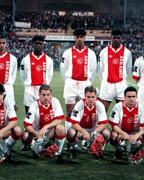 Ajax-selectie poseert voor een groepsfoto in het stadion, met spelers in rood-witte shirts en de doelman links.