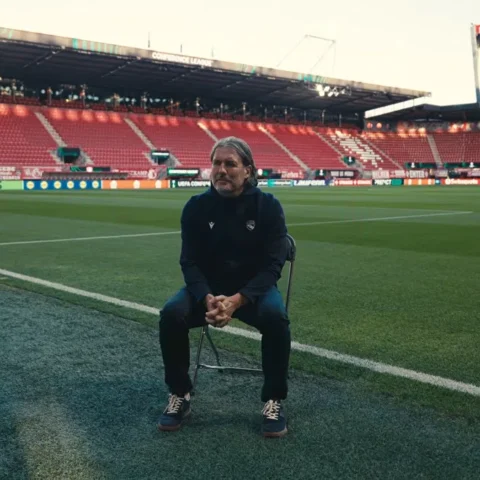 Andres Gerber zit op een inklapstoel op het veld in een leeg voetbalstadion.
