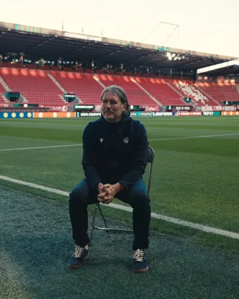 Andres Gerber zit op een inklapstoel op het veld in een leeg voetbalstadion.