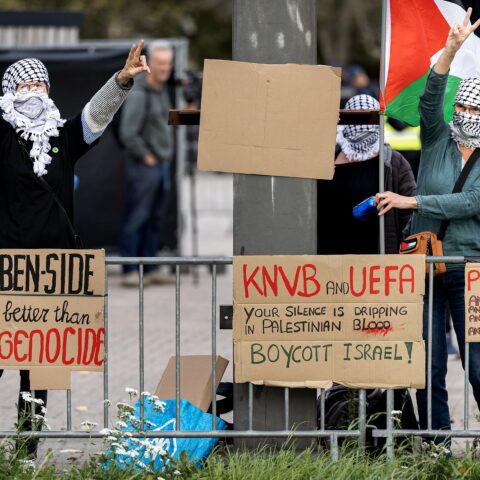 Protesters met gezichtsbedekking en Palestijnse vlag bij een afzetting, met borden tegen Israël en AZ.