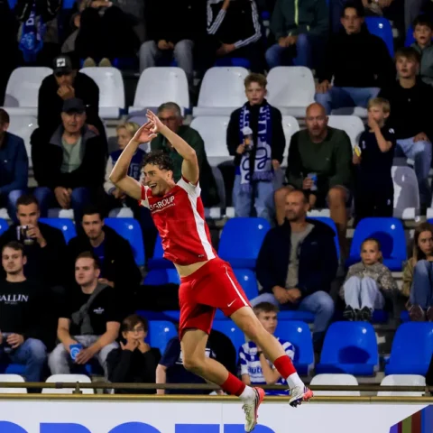 Voetballer in rood-wit juicht voor het publiek in een stadion.
