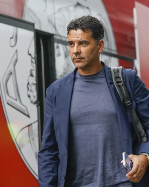 Míchel Sánchez loopt naast een rood teambusvoertuig met een tas over zijn schouder.