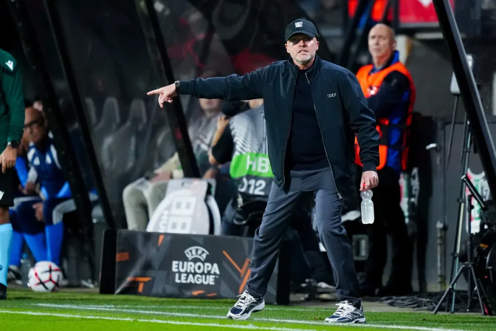 Dick Schreuder wijst langs de zijlijn tijdens een Europa League-wedstrijd.