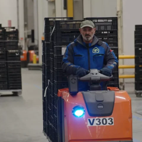 Medewerker rijdt met een elektrische magazijntruck tussen stellingen en rolcontainers in een distributiehal.