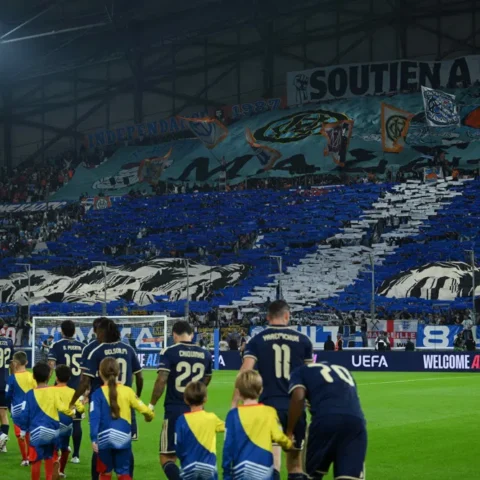 Spelers van Olympique Marseille lopen het veld op voor een vol vak met supporters en een grote stadiontifo.
