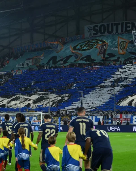 Spelers van Olympique Marseille lopen het veld op voor een vol vak met supporters en een grote stadiontifo.