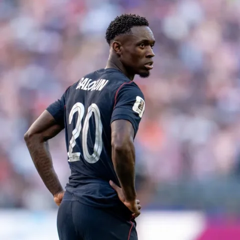 Folarin Balogun in een donker voetbalshirt met nummer 20, staand op het veld en omkijkend.