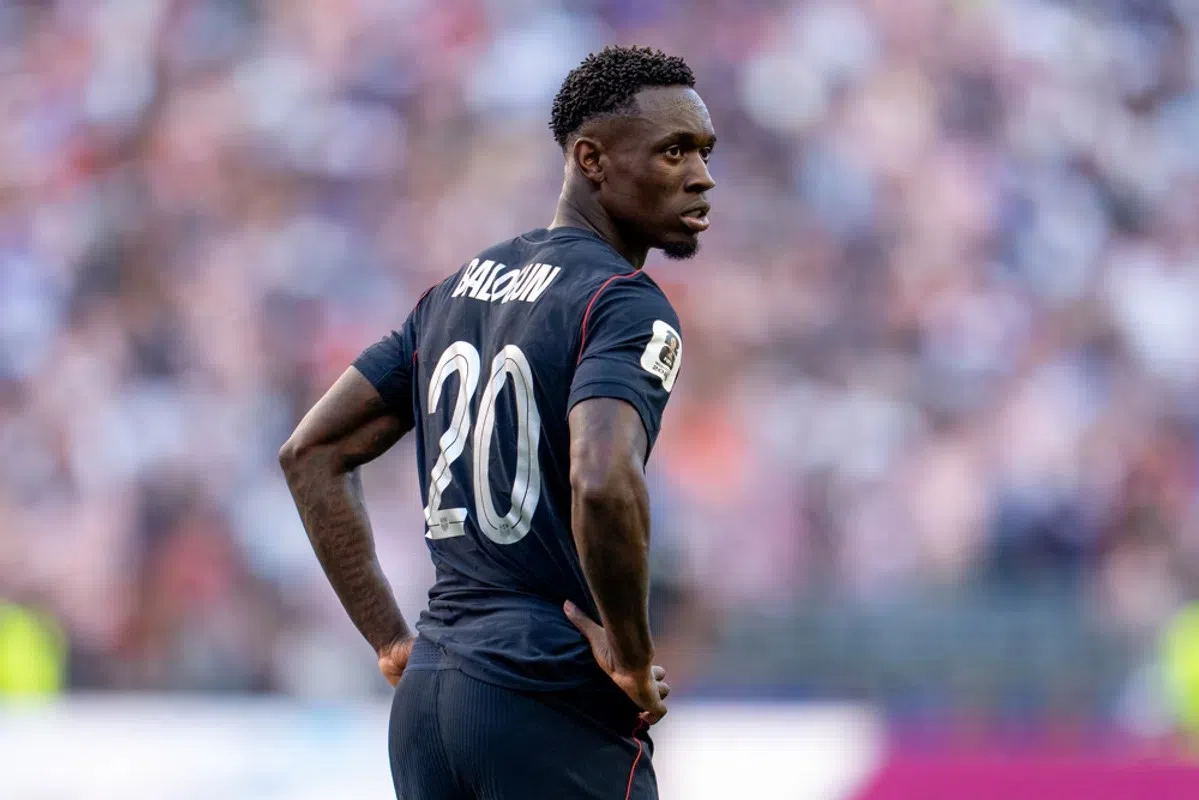 Folarin Balogun in een donker voetbalshirt met nummer 20, staand op het veld en omkijkend.