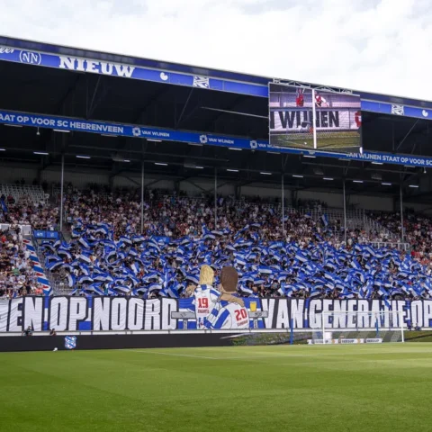 Supporters van SC Heerenveen in een vol vak in het Abe Lenstra Stadion met blauwe spandoeken en vlaggen.