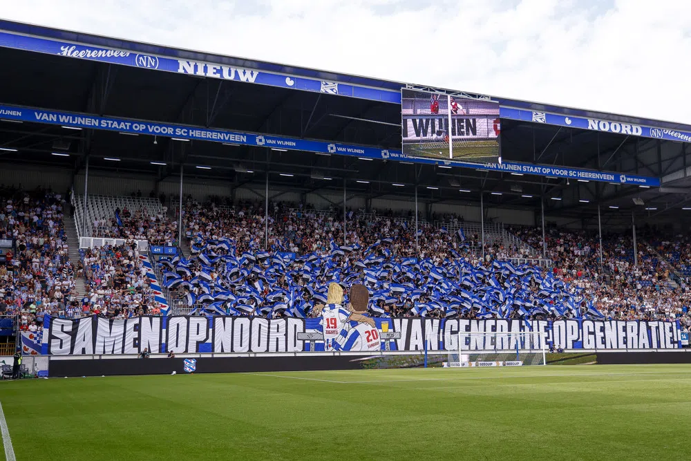 Supporters van SC Heerenveen in een vol vak in het Abe Lenstra Stadion met blauwe spandoeken en vlaggen.