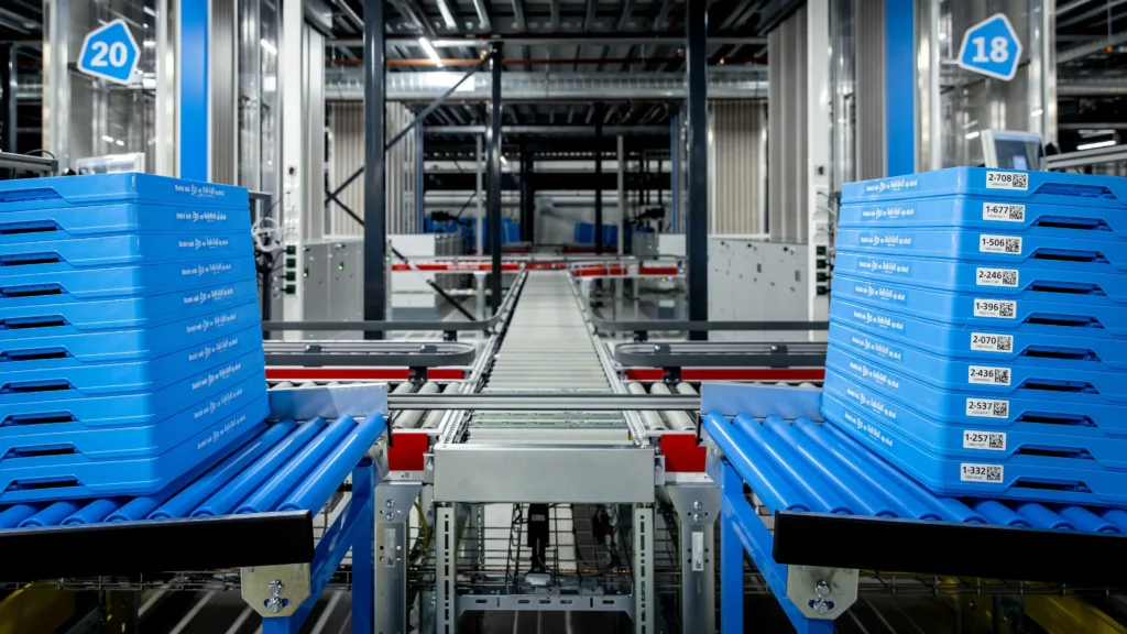 Blauwe Albert Heijn-bakken op een geautomatiseerde transportband in een distributiecentrum.