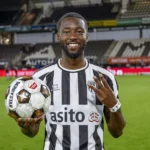 Een lachende Heracles Almelo-speler poseert op het veld met een voetbal.