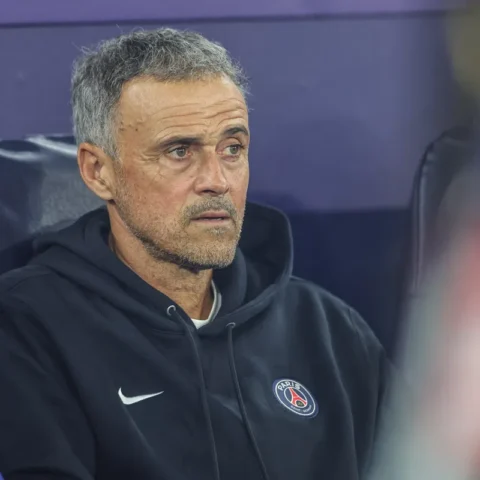 Luis Enrique zit op de bank in een PSG-trui en kijkt geconcentreerd vooruit.