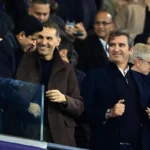 Manchester City-functionarissen staan lachend in de tribune tijdens een wedstrijd.