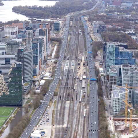 Luchtfoto van de Zuidas in Amsterdam met spoorlijnen, wegen, kantoren en werkzaamheden langs het Zuidasdok-traject.