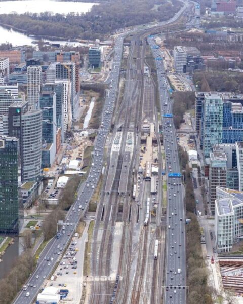 Luchtfoto van de Zuidas in Amsterdam met spoorlijnen, wegen, kantoren en werkzaamheden langs het Zuidasdok-traject.