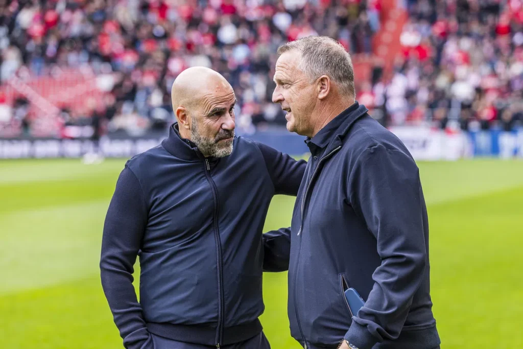 Peter Bosz en John van den Brom praten langs de zijlijn op een voetbalveld.
