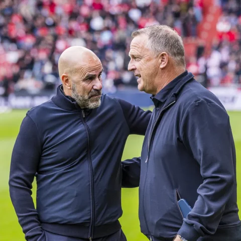 Peter Bosz en John van den Brom praten langs de zijlijn op een voetbalveld.